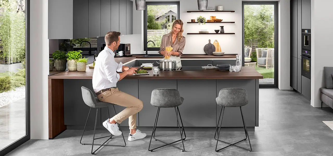 Ein Mann und eine Frau bereiten zusammen Essen in einer modernen grauen Küche mit Kücheninsel zu.