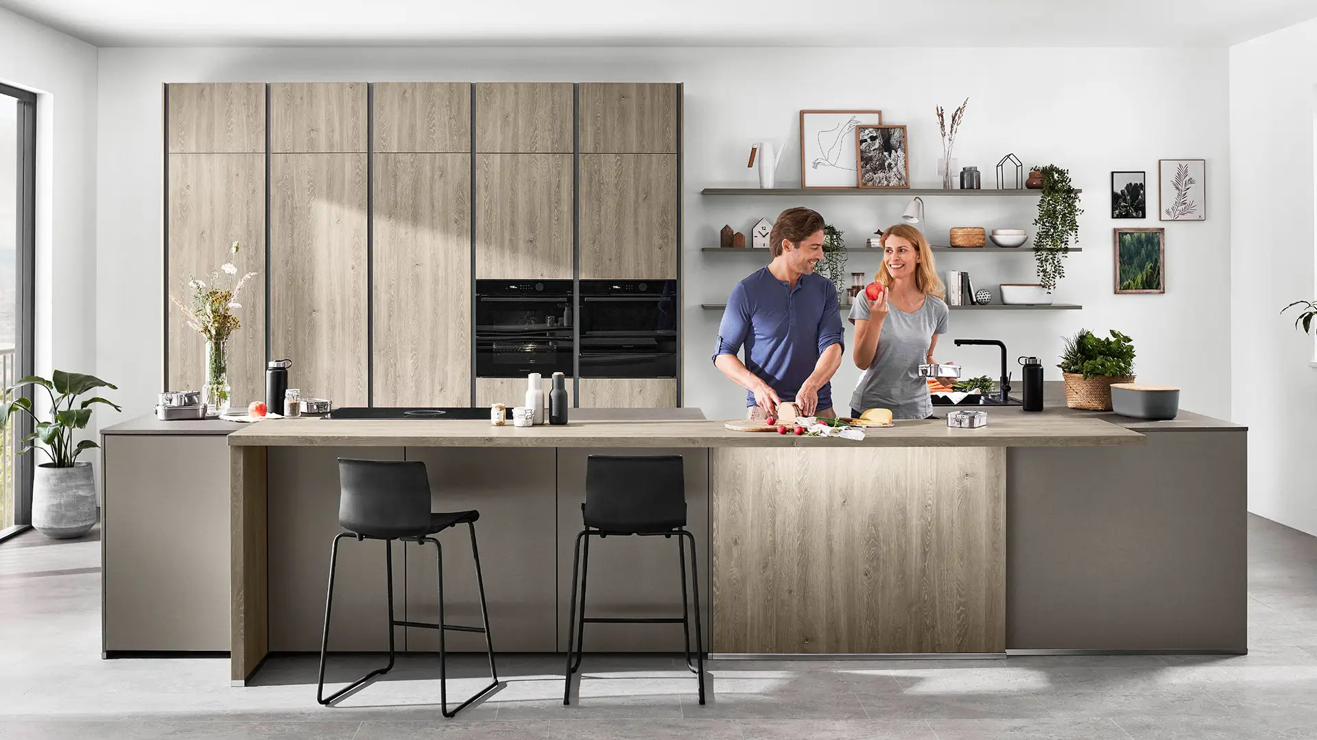 Modern helle Küche mit Holzfronten, zwei Personen kochen gemeinsam an der Kücheninsel.