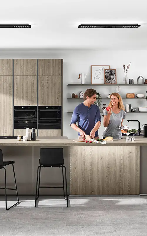 Paar bereitet gemeinsam Essen in moderner Küche mit Holzfronten und Kochinsel vor.